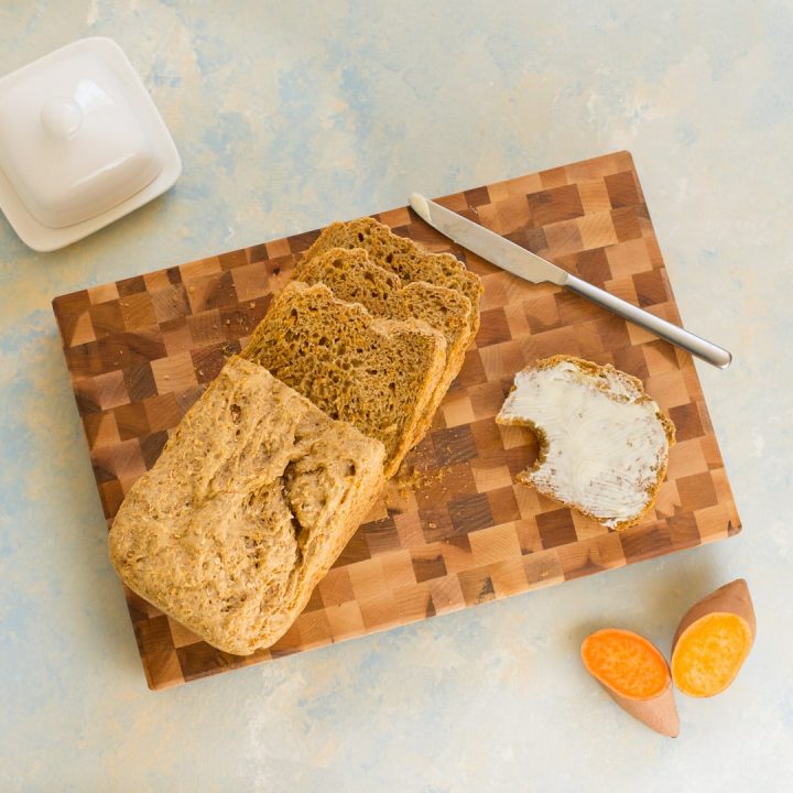 Saftiges Vollkornbrot mir viel Gemüse (Süßkartoffel), in Scheiben geschnitten auf einem Holzbrett