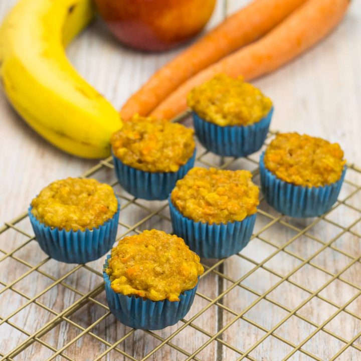 Muffins für Babys, auf einem Kuchenrost, dahinter liegen Bananen, Karotten und Äpfel