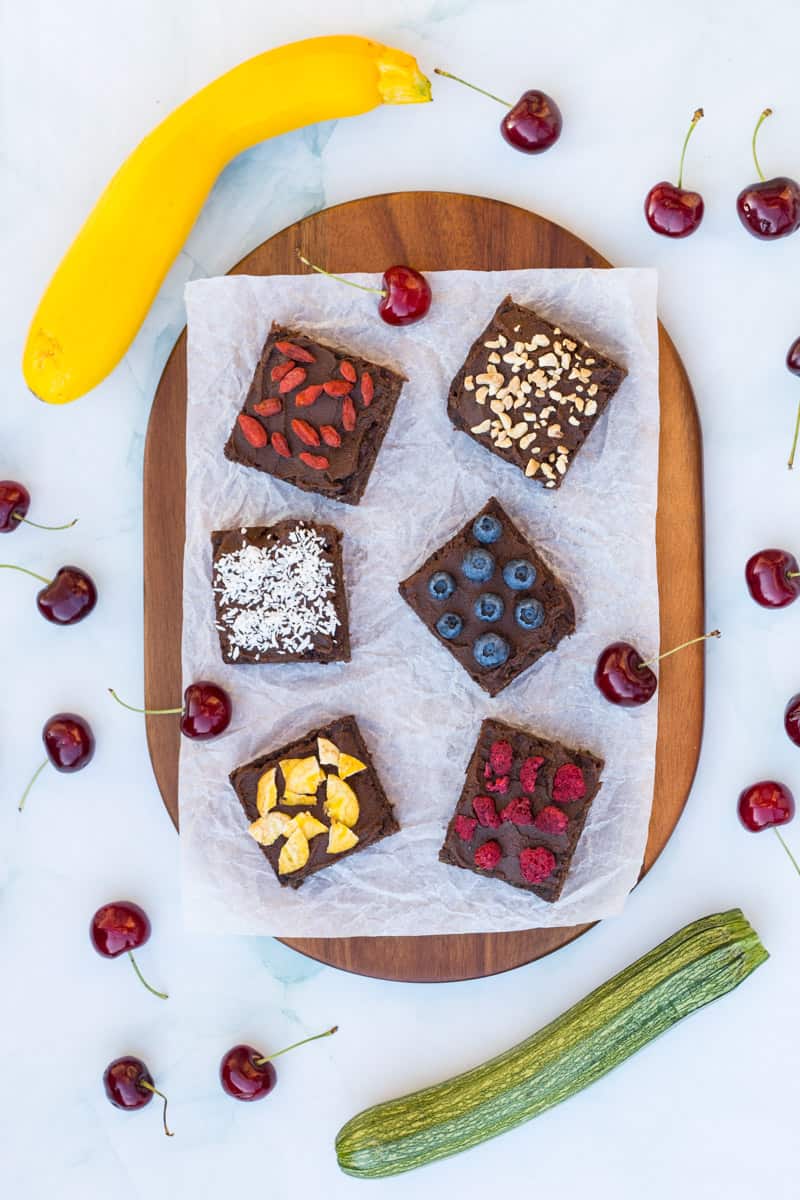 Zucchini-Muffins mit gesunder Schokocreme, verziert mit Beeren, Nüssen und anderen Toppings, auf einem Holzbrett