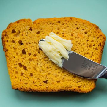 Eine Scheibe Süßkartoffelbrot ohne Hefe, auf einem Teller mit einem Messer und Butter