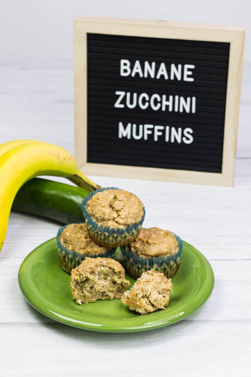 Zucchini-Muffins auf einem Teller gestapelt, dahinter liegt eine Zucchini und eine Banane