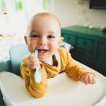 Baby im Hochstuhl, spielt mit einem Plastiklöffel