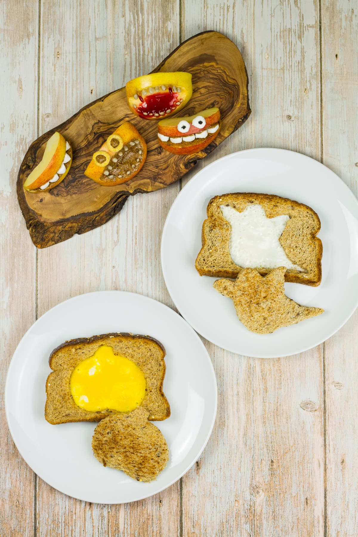 Frühstück zu Halloween, Toastscheiben die mit Kürbis und Geist ausgestochen und dann mit Ei gefüllt sind, dazu Münder aus Apfel.