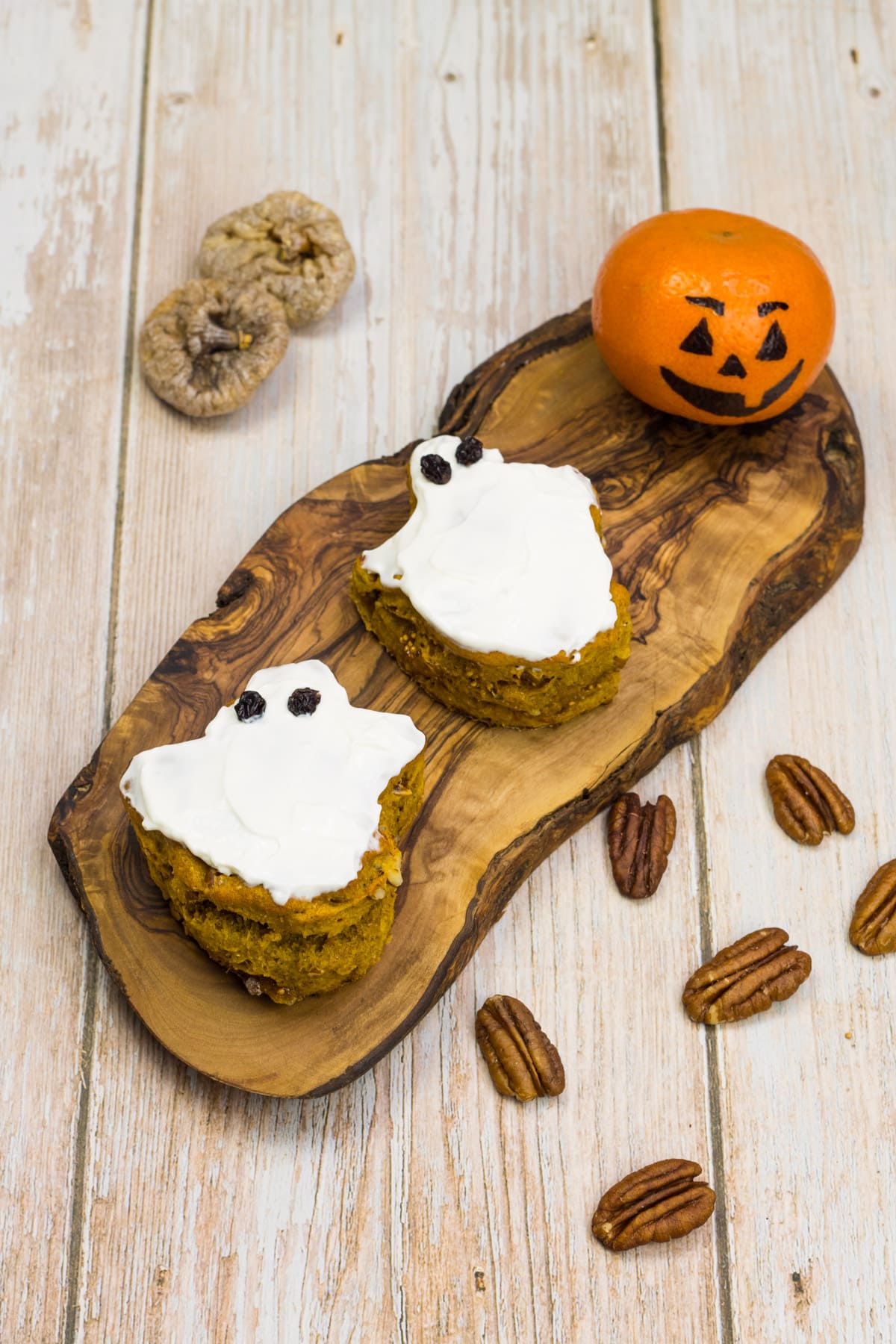 Scones als Geister ausgestochen, mit Frischkäse beschmiert und Rosinen als Augen, auf einem Holzbrett, als Halloween-Snack für Kinder