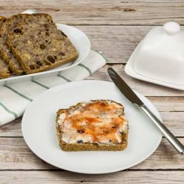 Eine Scheibe Brot mit Nüssen und Rosinen, auf einem Teller und beschmiert mit Butter und Marmelade