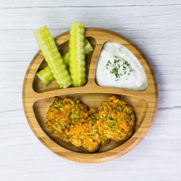 Gemüsepuffer mit Zucchini und Süßkartoffel, auf einem Babyteller, dazu Gurke und Dip