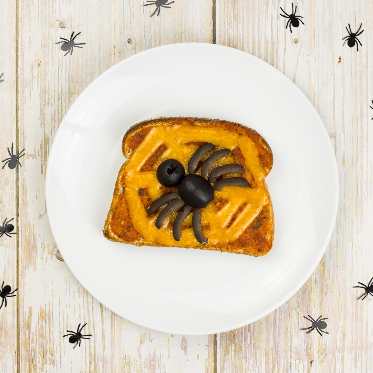 Toastbrot mit Tomatensoße, einem Spinnennetz aus Käse und einer Spinne aus schwarzen Oliven