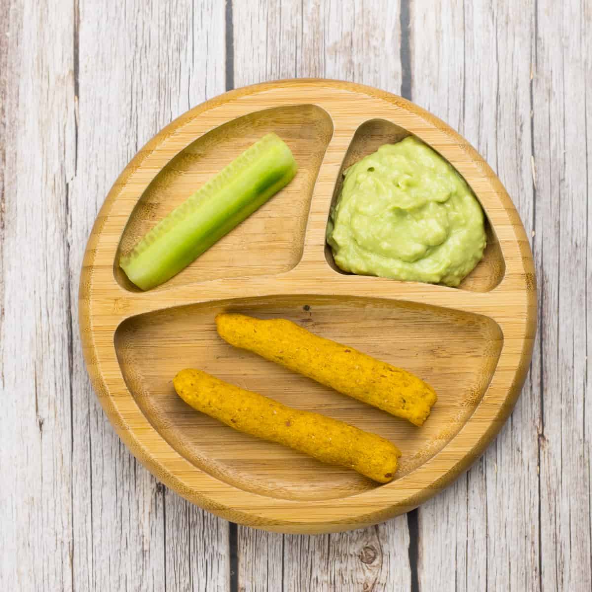 Schneller Avocado-Dip für Babys, auf einem Babyteller, mit Dinkelstangen und Gurke