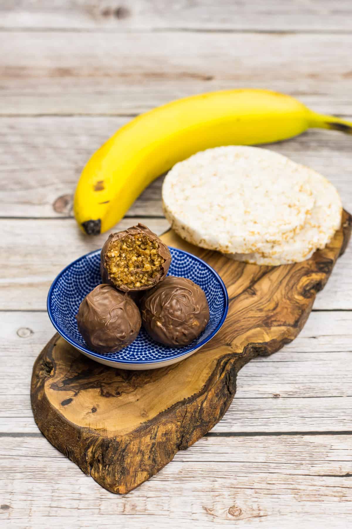 Puffpralinen, ein gesunder Snack aus gepufftem Reis, auf einem Teller gestapelt, dahinter Reiswaffeln und Banane