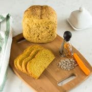 Karottenbrot für Babys, mit gemahlenen Sonnenblumenkernen, aufgeschnitten auf einem Holzbrett, daneben eine Möhre und Sonnenblumenkerne