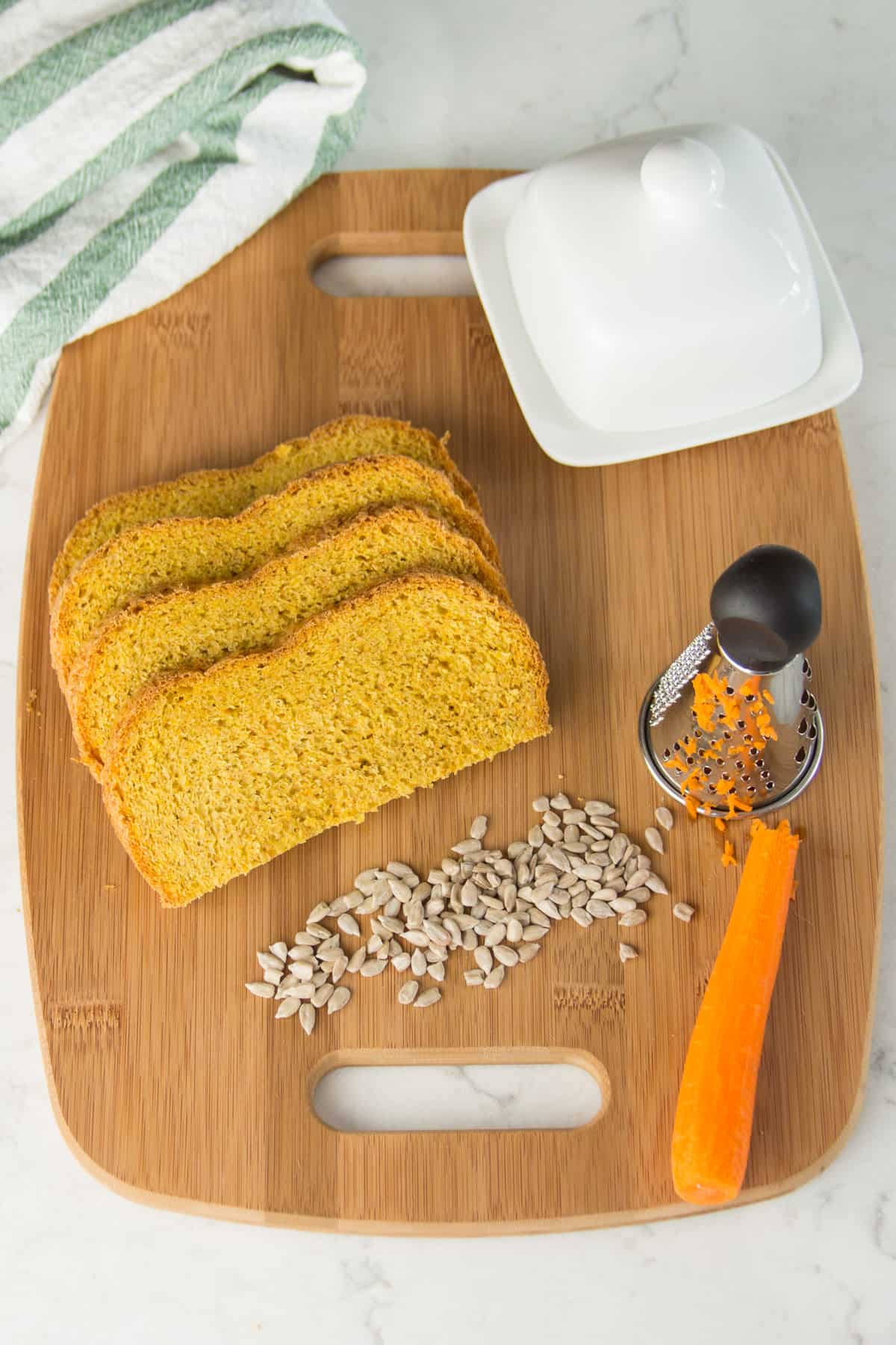 Karottenbrot für Babys, mit gemahlenen Sonnenblumenkernen, aufgeschnitten auf einem Holzbrett, daneben eine Möhre und Sonnenblumenkerne