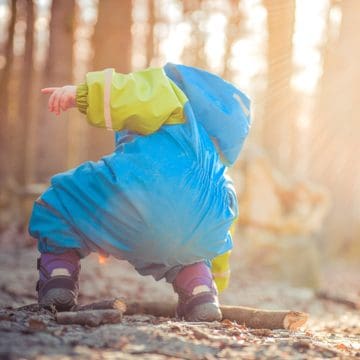 Kleinkind im Wald, hebt einen Stock vom Boden auf