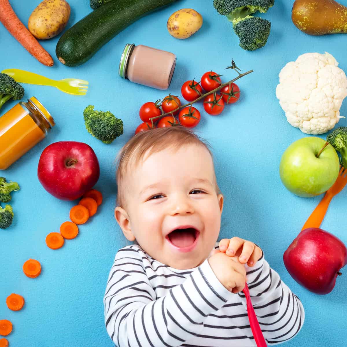 Baby liegt mit Rücken auf dem Boden und ist umgeben von Gemüse und Obst