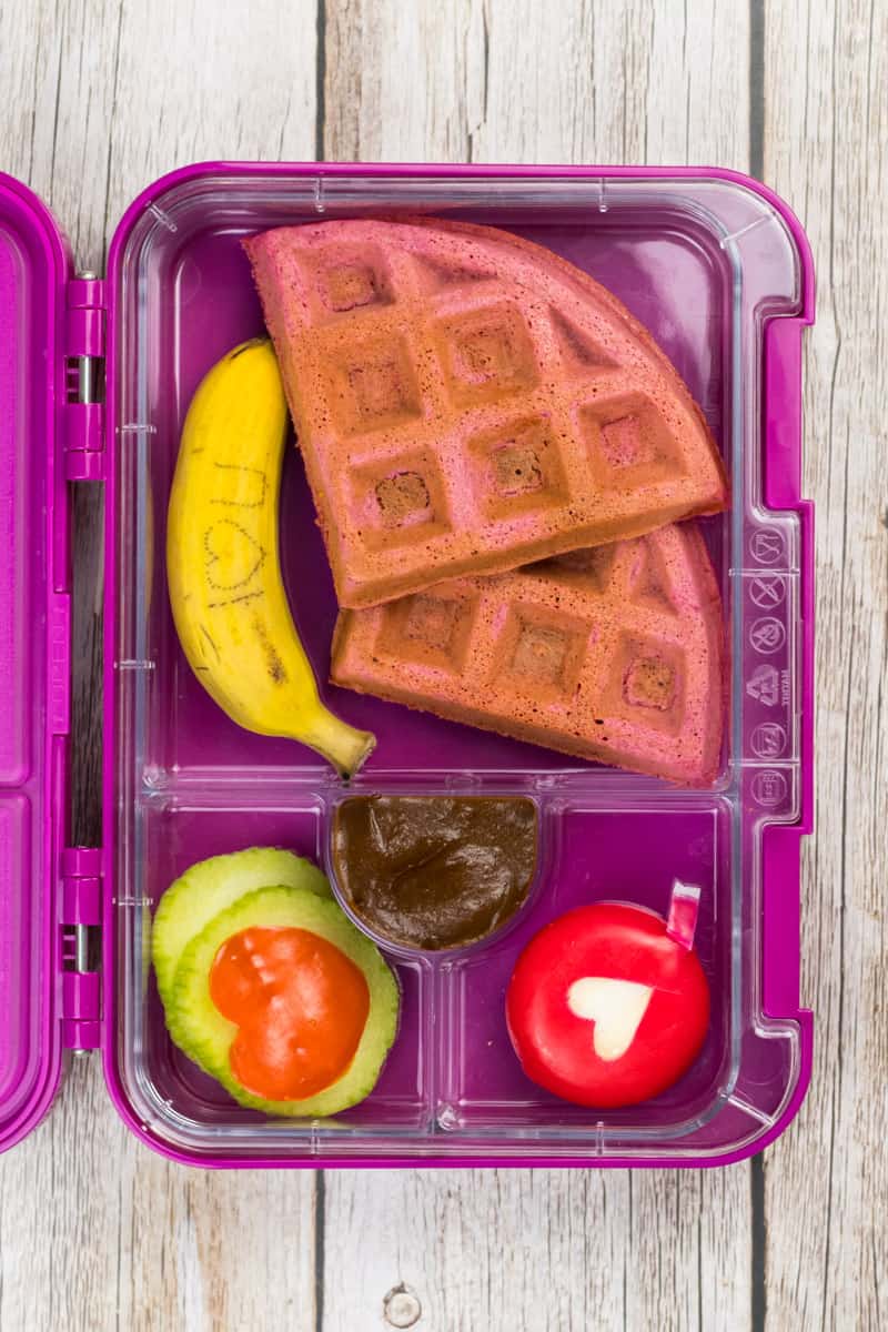 Eine Ich liebe Dich Bentodose mit pinken Waffeln, einer Babybanane, einem Käse und Gurke und Paprika zu Herzen ausgestochen