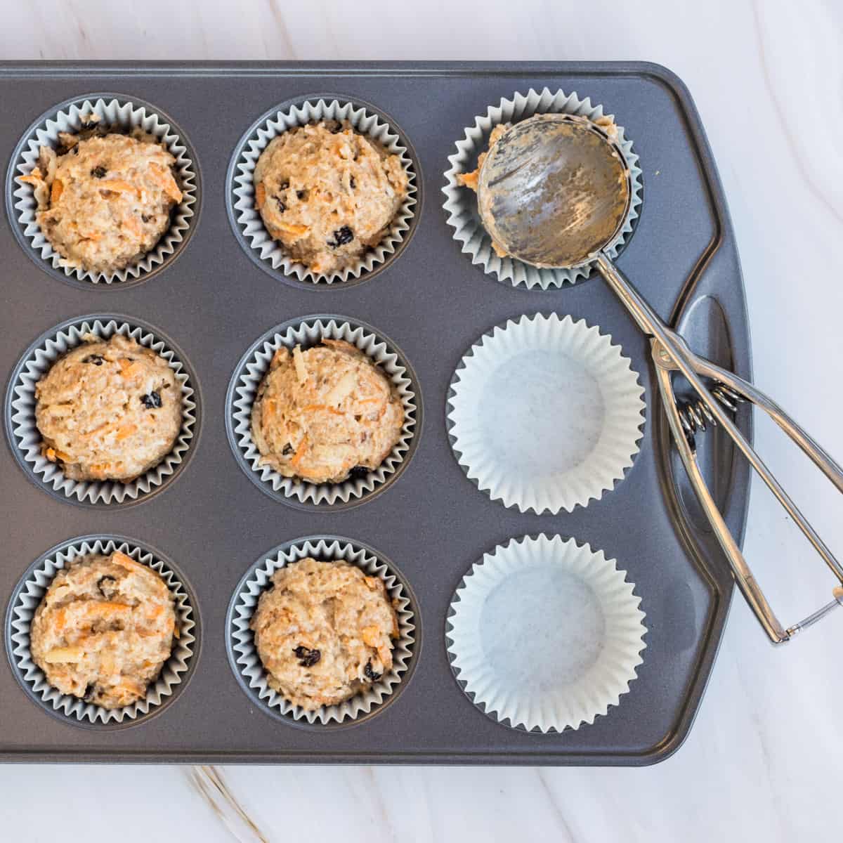 Teig für süße Frühstücksmuffins auf eine Muffinform verteilt, mit einem Eisportionierer