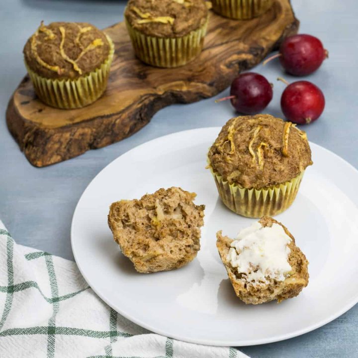 Saftiger Apfelmuffin ohne Zucker, auf einem Teller, in zwei Hälften gebrochen, eine Hälfte ist mit Butter bestrichen