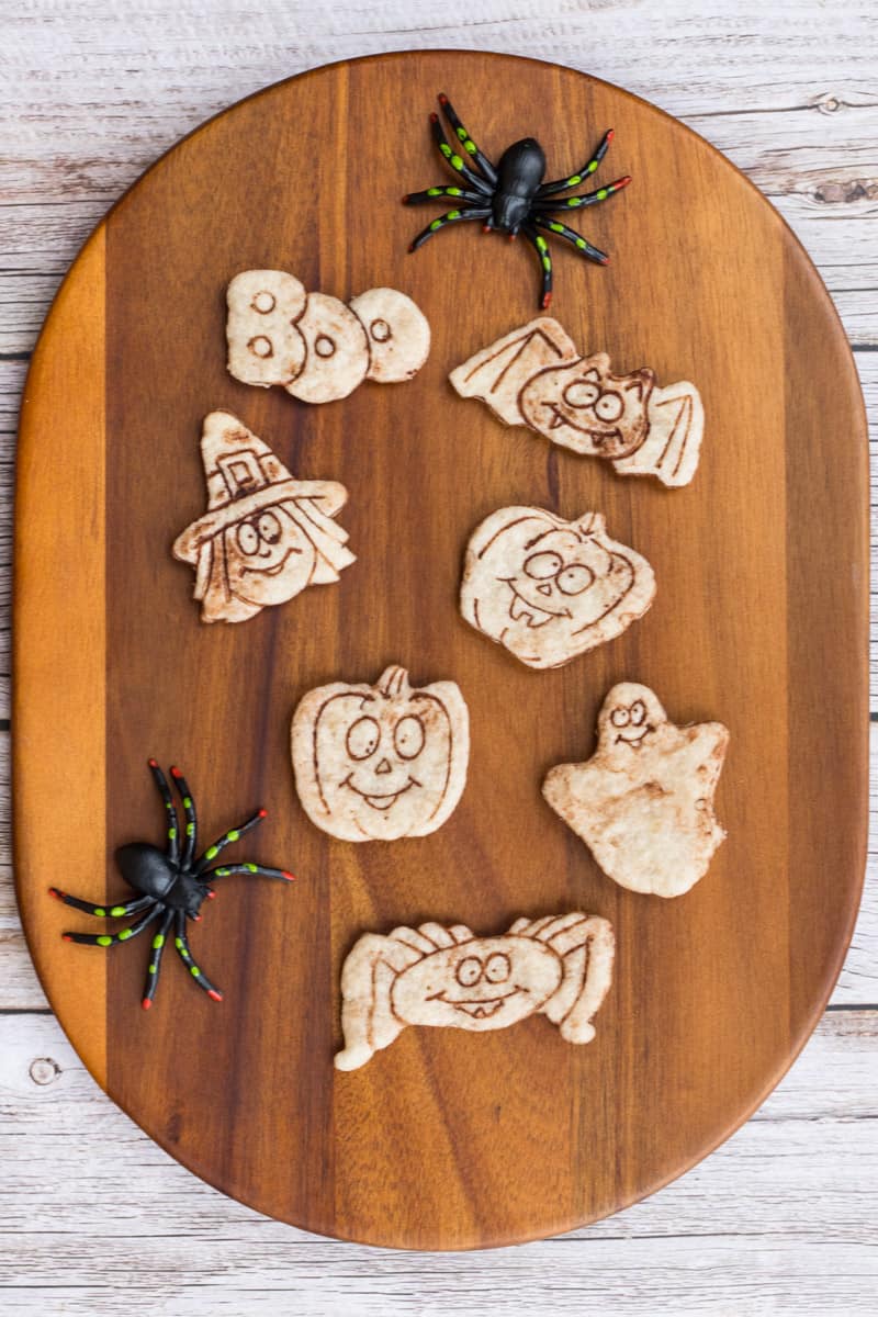 Zuckerfreie Halloween-Kekse mit 3D Keksformen ausgestochen, auf einem Holzbrett, daneben sind zwei Spinnen.