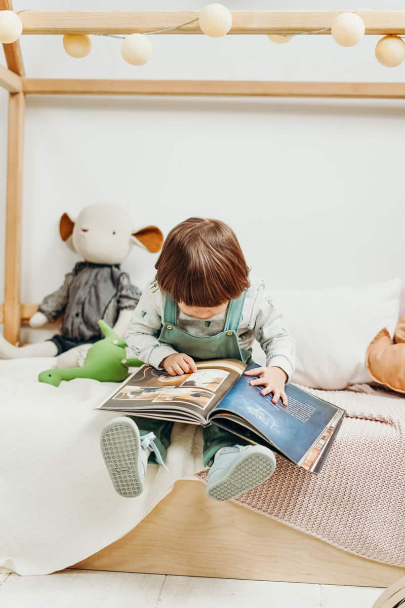 Kleinkind sitzt auf dem Bett und blättert in einem Buch