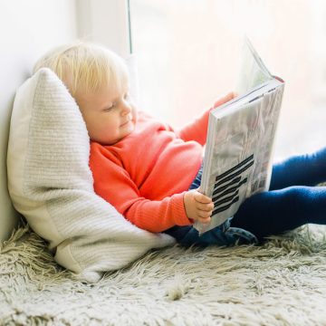 Kleinkind hält ein Buch auf dem Schoß und blättert darin