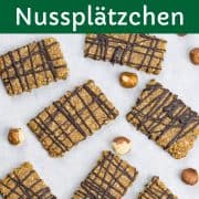 Nussplätzchen mit Schokolade, auf einem Stück Backpapier, mit Haselnüssen daneben