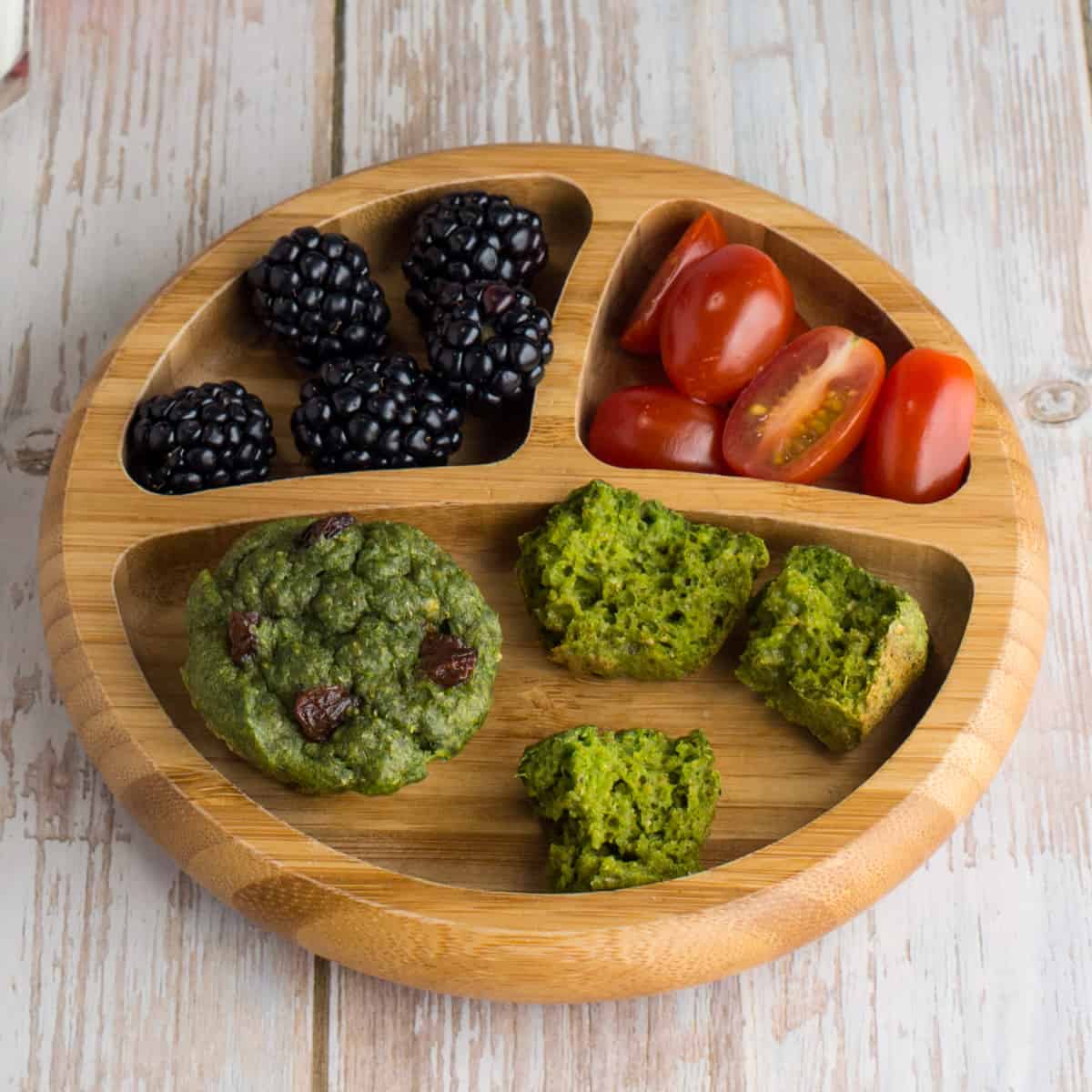 Zuckerfreie Bananenmuffins mit Spinat, auf einem Babyteller, mit Brombeeren und geviertelten Tomaten