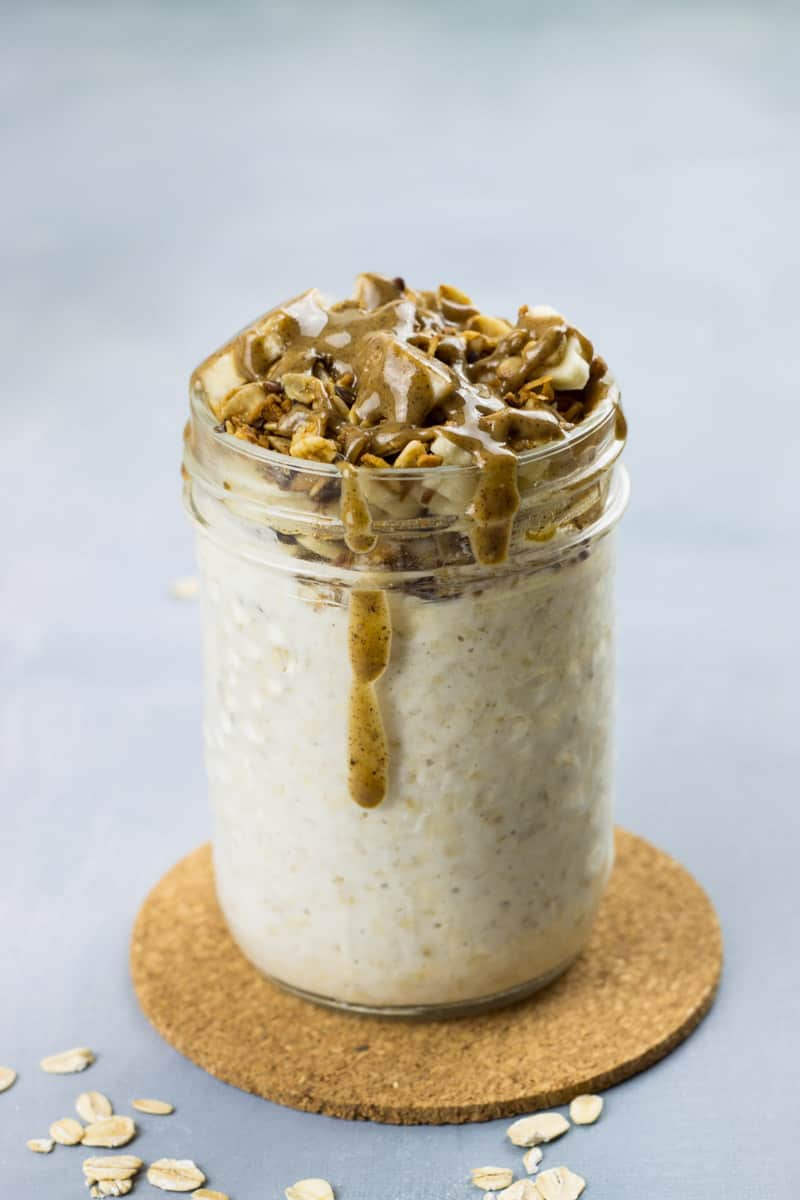 Overnight Oats mit Joghurt, sowie Banane, Granola und Nussmus als Topping, in einem Glas