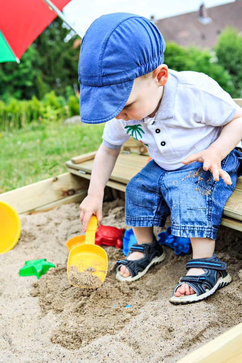 Kleinkind spielt in Sandkiste, buddelt mit einer Schaufel Sachen aus