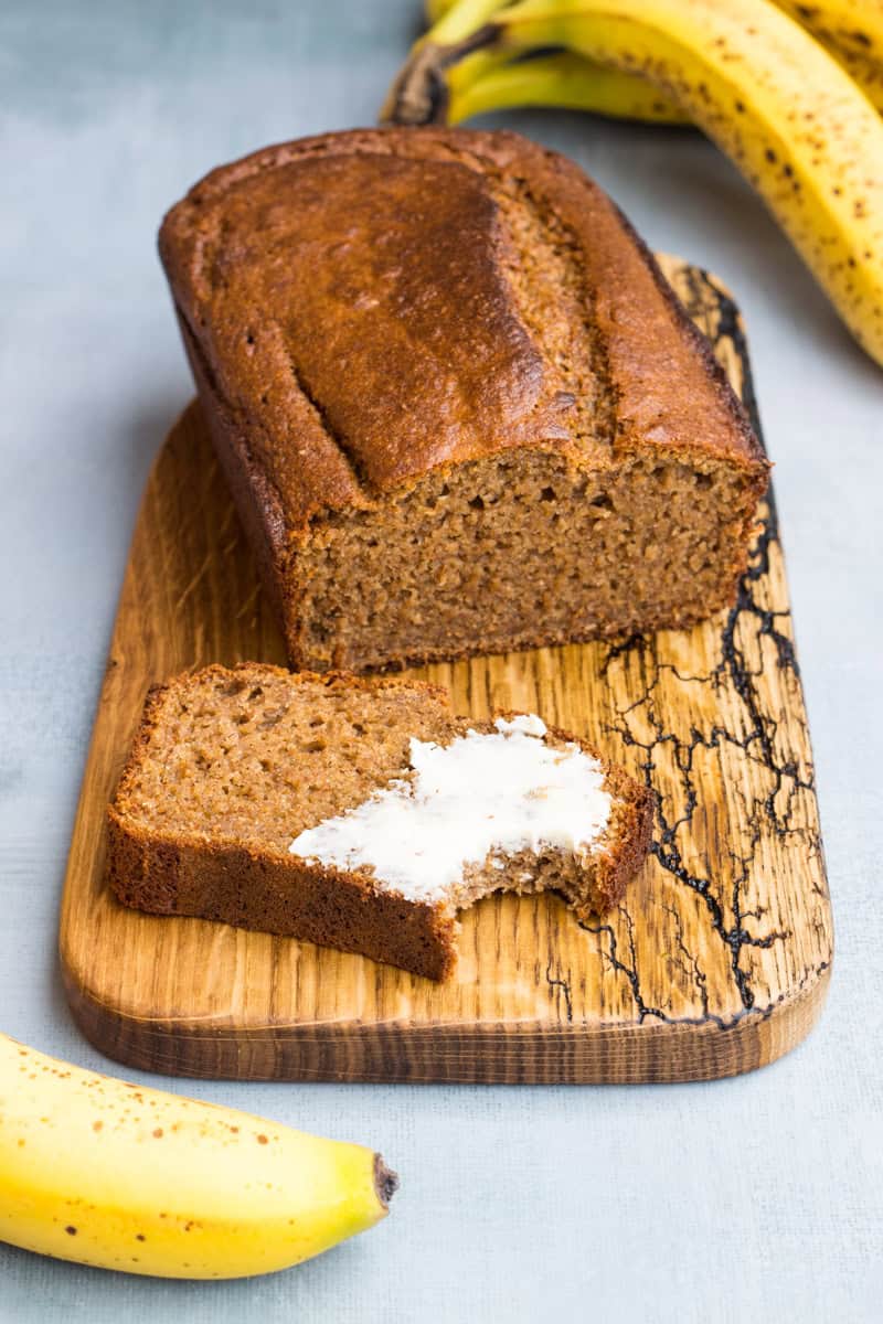 Bananenbrot, aufgeschnitten auf einem Holzbrett, eine Scheibe ist mit Butter beschmiert