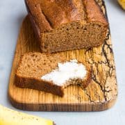 Bananenbrot, aufgeschnitten auf einem Holzbrett, eine Scheibe ist mit Butter beschmiert