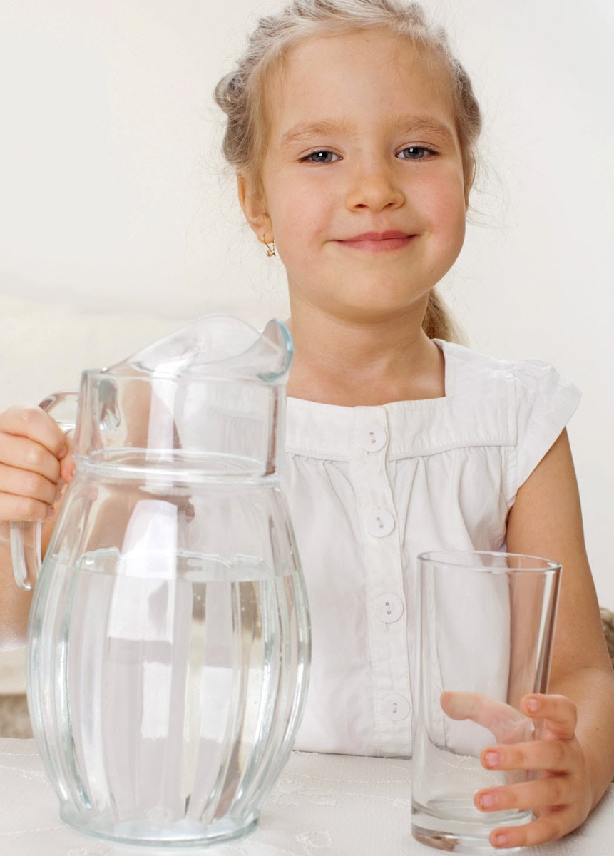 Mädchen mit einer Karaffe voll Wasser und einem leeren Trinkglas, schenkt sich selber Wasser ein