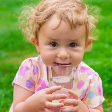 Kleinkind hält ein Glas Wasser in der Hand und trinkt daraus