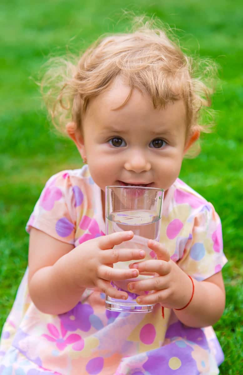 Kleinkind hält ein Glas Wasser in der Hand und trinkt daraus