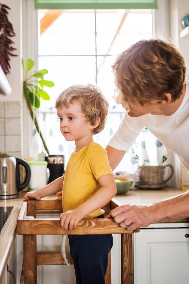 Vater und Sohn stehen am Herd und kochen zusammen, dabei steht das Kind auf einem Lernturm