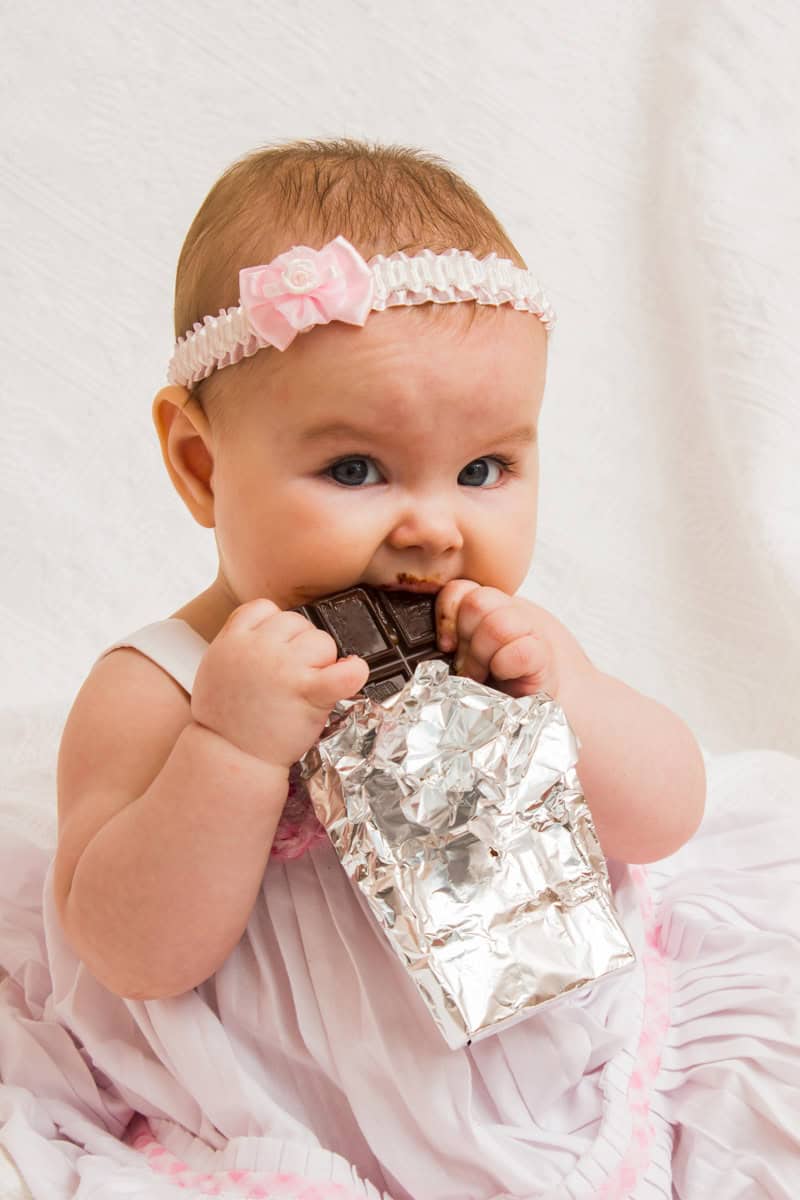 Baby steckt eine Tafel Schokolade in den Mund, obwohl Babys noch keine Süßigkeiten bekommen sollten