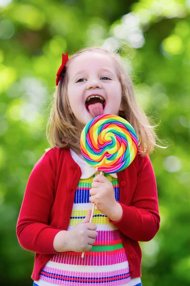 Kleines Mädchen mit einem großen Lolli in der Hand, an dem es leckt