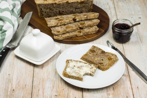 Saftiges Vollkornbrot mit getrockneten Feigen und Walnüssen, einfach und ohne Kneten, auf einem Teller mit Butter bestrichen