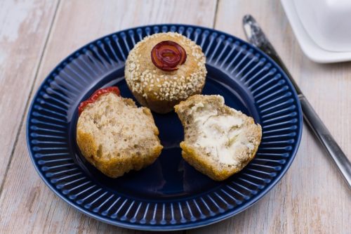 Focaccia Brötchen bzw. Muffin auf einem Teller, ein luftiges Vollkornbrötchen ist in zwei Hälften geteilt und eine Hälfte mit Butter beschmiert.